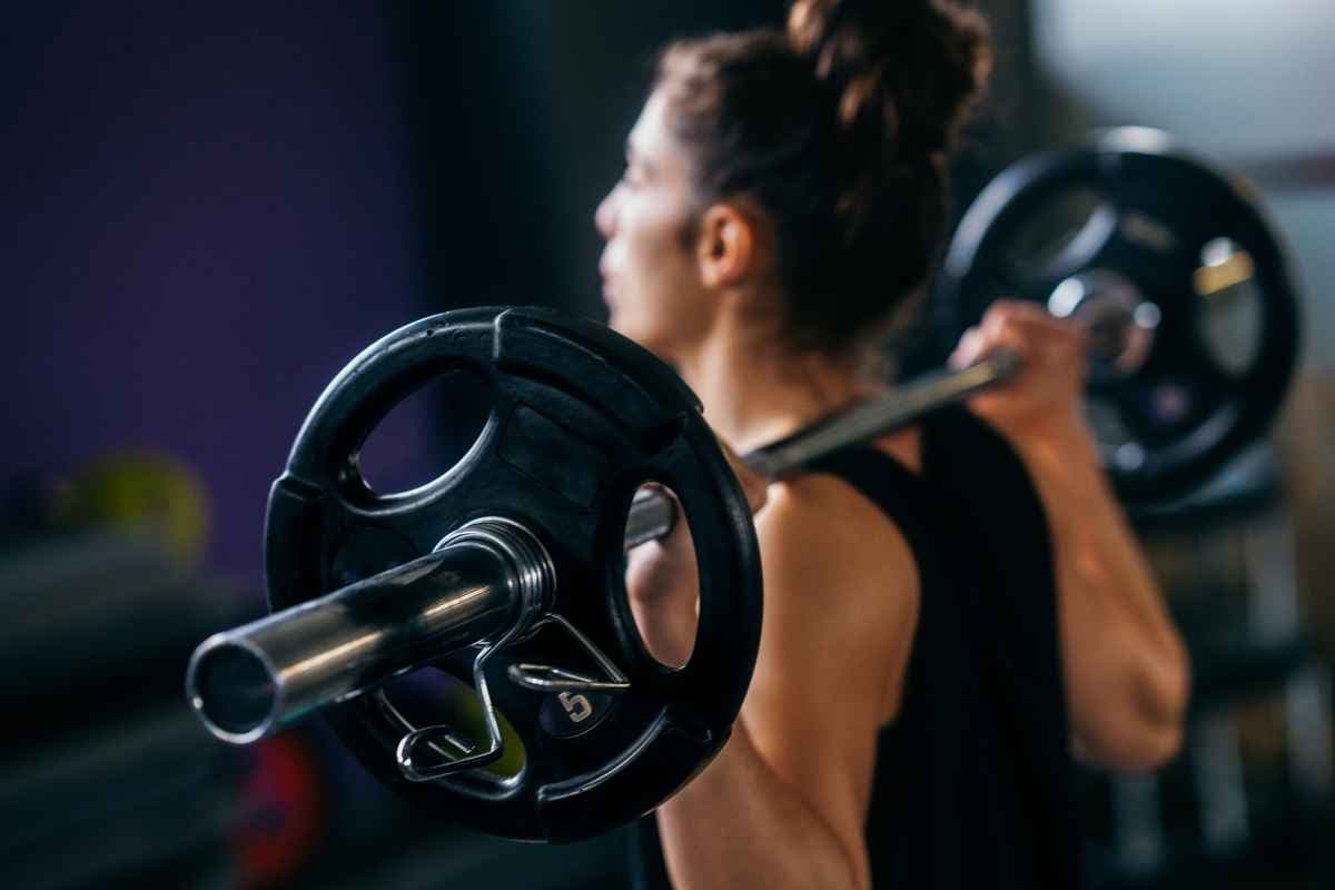 A woman lifting a loaded barbell across her shoulders in a gym.