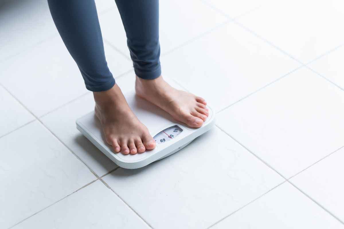 Bare feet standing on white bathroom scales on a tiled floor.