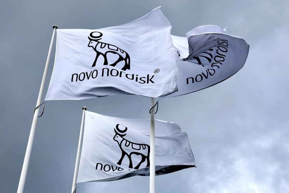 Three Novo Nordisk flags flying against an overcast grey sky.