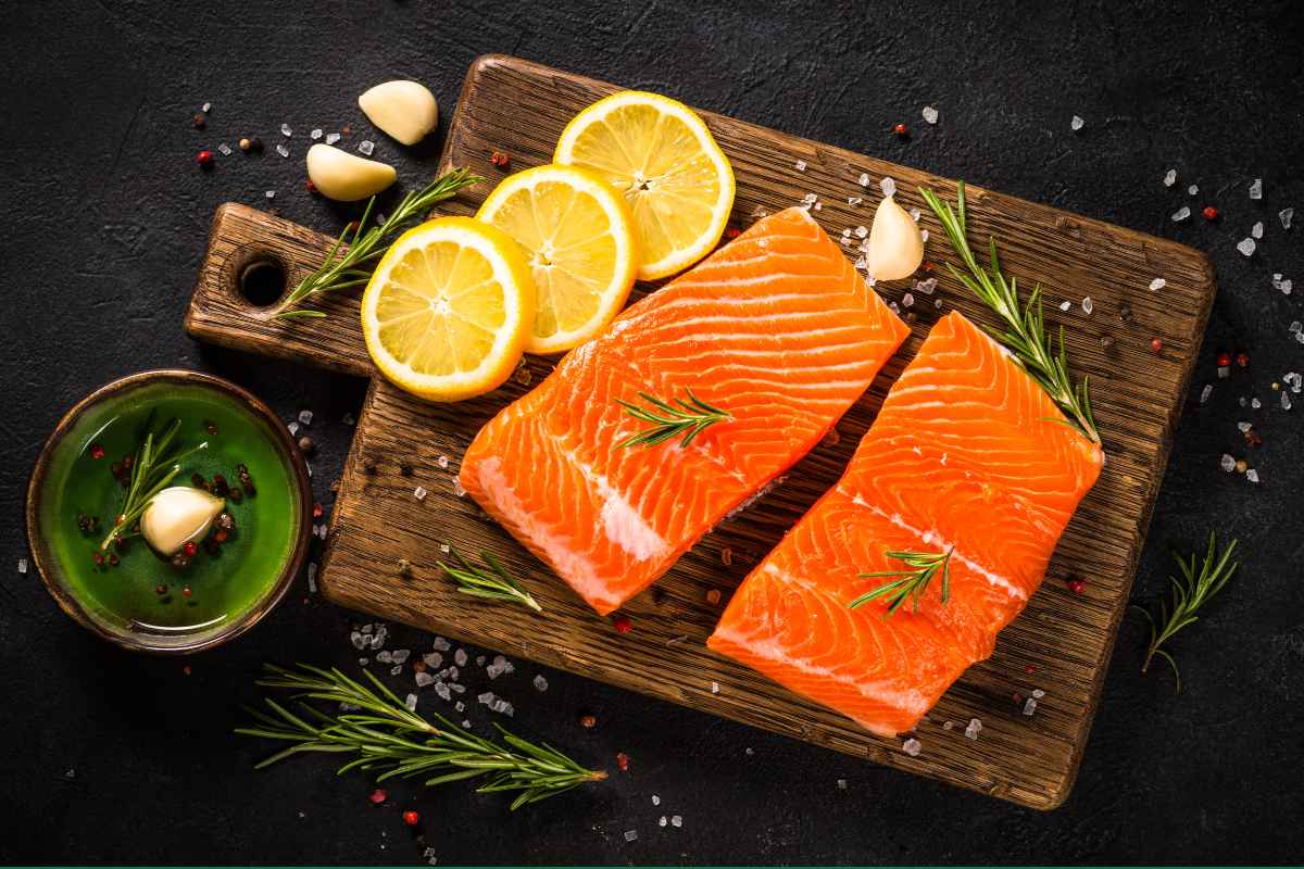 Two raw salmon fillets on a wooden board with lemon slices, rosemary and garlic.
